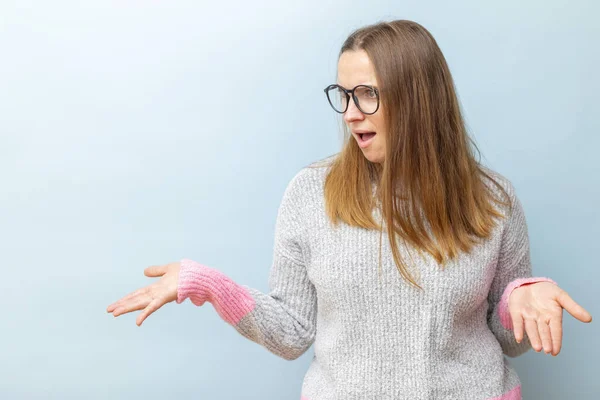 A woman in eyeglasses expressing surprise with a confused gesture against a light blue background.