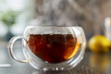 Sıcak, dumanı tüten bir fincan çayın yakın planda bulanık bir arka planı olan ahşap bir masada..