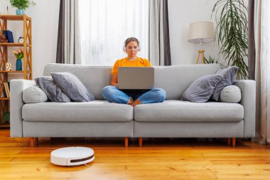 Odaklanmış bir kadın koltukta bağdaş kurup kulaklıklı bir dizüstü bilgisayarla uzaktan kumandalı iş yaşam tarzını somutlaştırıyor..