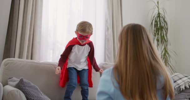 Kind Superheldenkostüm Spielt Mit Begeisterter Mutter Einer Hellen Wohnzimmerkulisse Hochwertiges — Stockvideo