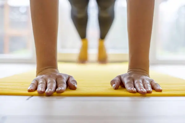 Hands pressed flat on yellow yoga mat, workout session indoors.