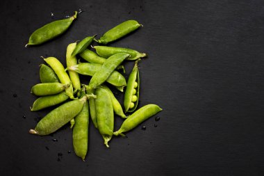 Taze yeşil bezelye kabukları koyu bir arkaplana saçılmış, bazı açık bezelyeler içinde.