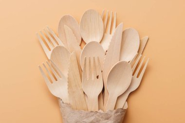 Bej bir arka planda kağıt torba içinde biyolojik olarak çözünür tahta kaşıklar ve çatallar..