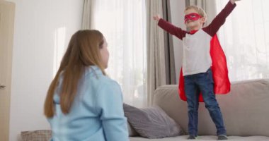 Süper kahraman kostümlü çocuk evde annesiyle oynuyor. Sıradan aile eğlencesi konsepti. Yüksek kalite 4k görüntü