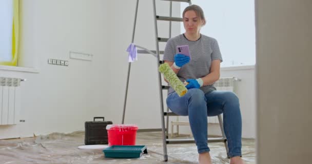 Уставшая Женщина Сидящая Лестнице Разговаривая Телефону Рулоном Краски Руке Возможно — стоковое видео