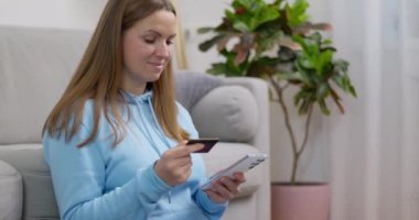 Evde online alışverişler için akıllı telefon ve kredi kartı kullanan mavi kapüşonlu bir kadın. Yüksek kalite 4k görüntü