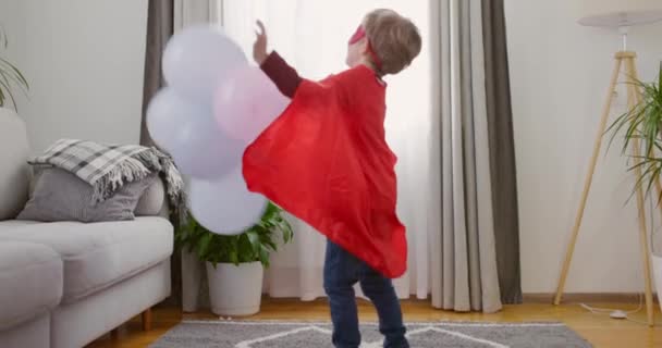 Dziecko Kostiumie Superbohatera Czerwoną Peleryną Maską Bawiące Się Balonami Otoczeniu — Wideo stockowe