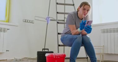 Merdivende oturan yorgun bir kadın, elinde boya silindiriyle telefonda konuşuyor, muhtemelen profesyonel yenileme yardımı istiyor. Yüksek kalite 4k görüntü
