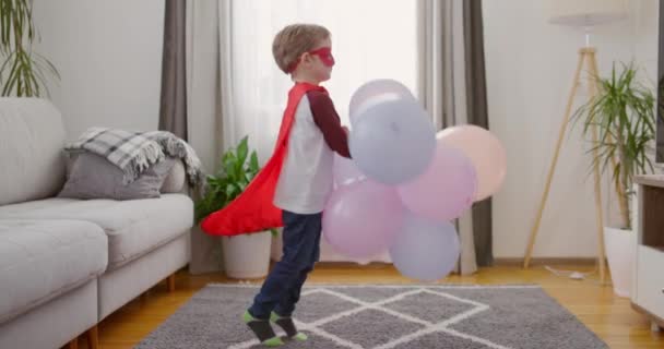 Маленький Ребенок Костюме Супергероя Играет Красочными Воздушными Шарами Уютной Гостиной — стоковое видео