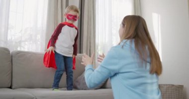 Süper kahraman kostümlü çocuk evde annesiyle oynuyor. Sıradan aile eğlencesi konsepti. Yüksek kalite 4k görüntü