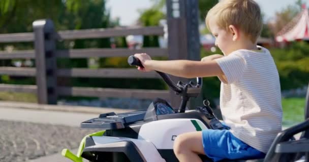 Młody Chłopiec Luźnym Letnim Stroju Jeździ Elektrycznym Zabawkowym Samochodem Zewnątrz — Wideo stockowe