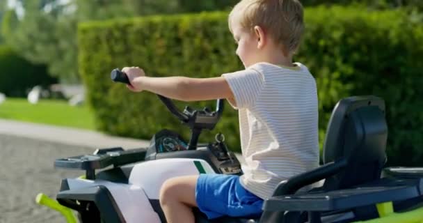 カジュアルな夏の服を着た少年は 晴れた日に屋外で電気玩具車を運転し 子供の頃の喜びと自由を体現しています 高品質の4K映像 — ストック動画