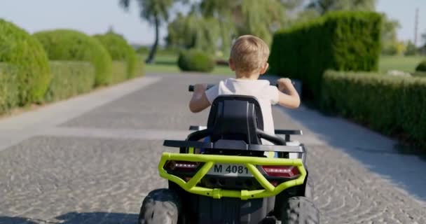 おもちゃの電気自動車に乗って日当たりの良い公園の道を眺める子供のバックビュー 高品質の4K映像 — ストック動画