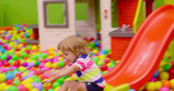 若い子供は 活気に満ちた屋内遊び場のボールピットにオレンジ色のスライドを下ろす遊び心のあるスライドを楽しんでいます 高品質の4K映像 — ストック動画