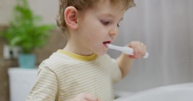 Genç bir çocuk banyoda diş fırçasıyla diş fırçalıyor. Yakın plan gizli çekim. Çocuk diş bakımı ve günlük rutin konsept. Yüksek kalite 4k görüntü