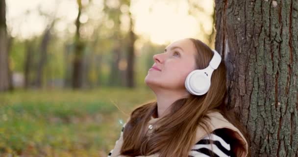Femme Appuyée Contre Arbre Écoutant Musique Sur Des Écouteurs Blancs — Video
