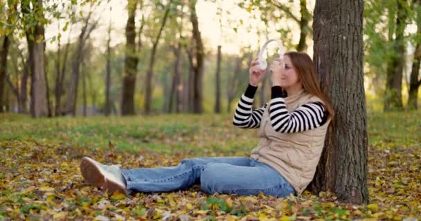 Γυναίκα Κάθεται Κάτω Από Ένα Δέντρο Στο Πάρκο Φθινόπωρο Πεσμένα — Αρχείο Βίντεο