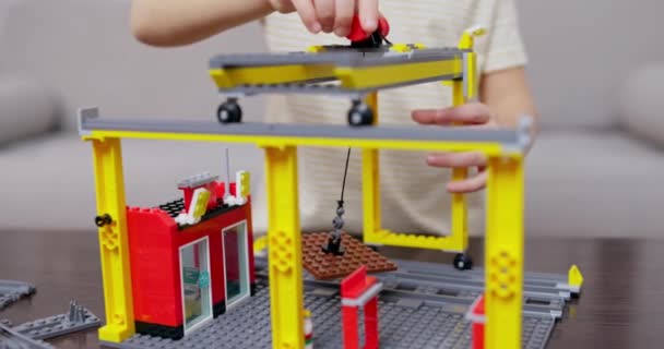 テーブルの上の活気に満ちた連結プラスチック ブロックのキットからの構造クレーンを組み立てる子供の手 高品質の4K映像 — ストック動画