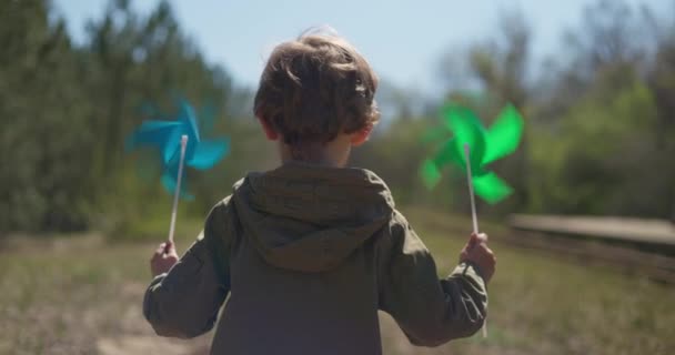 Widok Tyłu Dziecka Biegnącego Niebieskimi Zielonymi Pinwheels Film Zabawnym Momentem — Wideo stockowe