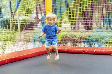 Mavi kıyafetli çocuk renkli trambolinde zıplıyor. Eğlenceli aktivite ve konsept. Pankart için tasarım, poster.