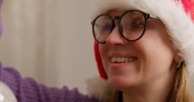 Noel Baba şapkalı bir kadının süslenmiş bir ağaca kırmızı bir Noel süsü asıp bayram neşesi saçtığı yakın plan. Yüksek kalite 4k görüntü