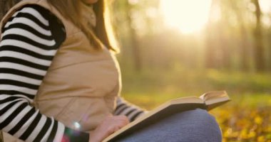 Sonbaharda yaprak serpiştirilmiş bir parktaki bir ağacın altında kitap okumaya dalmış genç bir kadının huzurlu bir sahnesi. Yüksek kalite 4k görüntü