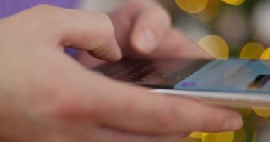 Sanal bir klavyeyle akıllı telefondan yazı yazan ellerin yakın çekimi. Arkaplanı bulanık, sarı bokeh ışıkları var. İletişim ve teknoloji kavramı. Yüksek kalite 4k görüntü