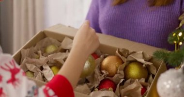 Bir anne ve oğulun Noel ağacını süslerken altın süsler asıp bayram mevsimini birlikte kutladıkları yakın plan. Yüksek kalite 4k görüntü