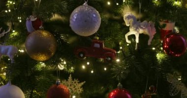 Kırmızı ve altın süslemeli Noel ağacı süslemeleri, oyuncak kamyon ve beyaz at heykelciği. Bayram ışıkları dalları aydınlatıyordu. Noel dekorasyonu ve kutlama konsepti