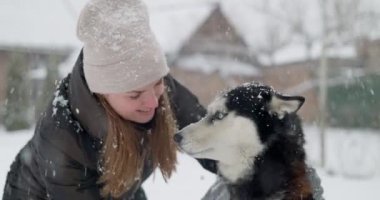Gülümseyen bir kadın, karlı bir günde açık havada köpeğiyle oynar, kış arkadaşlığının keyfini yakalar. Yüksek kalite 4k görüntü