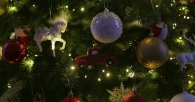 Kırmızı ve altın süslemeli Noel ağacı süslemeleri, oyuncak kamyon ve beyaz at heykelciği. Bayram ışıkları dalları aydınlatıyordu. Noel dekorasyonu ve kutlama konsepti