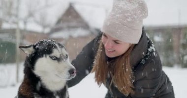 Gülümseyen bir kadın, karlı bir günde açık havada köpeğiyle oynar, kış arkadaşlığının keyfini yakalar. Yüksek kalite 4k görüntü