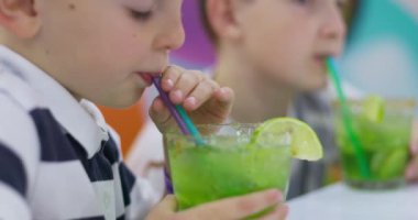Canlı bir restoran standında oturmuş, limonlu süslemeyle ferahlatıcı yeşil içkinin tadını çıkaran genç bir çocuk. Yüksek kalite 4k görüntü