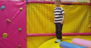 Canlı bir oyun sahasında, duvarlara tırmanma, köpük blokları ve parlak güvenlik ağlarıyla birlikte atlayan genç bir çocuk. Yüksek kalite 4k görüntü