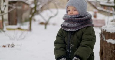 Soğuk bir günde, karla kaplı bir arka bahçede kar topu yuvarlayan, kışlık giysiler içinde sıcacık giyinmiş bir çocuk. Yüksek kalite 4k görüntü