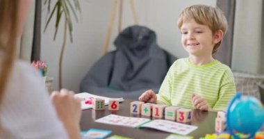 Çizgili tişörtlü gülümseyen genç, matematik blokları ve öğrenme materyalleri ile eğitici bir aktivite sırasında bir yetişkine beşlik çakıyor. Eğitim ve öğrenim faaliyetleri kavramı. Yüksek kalite 4k görüntü
