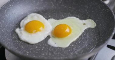 Yapışmayan bir tavada pişen iki güneşli yumurta, parlak sarılarını ve cızırtılı dokularını gözler önüne seriyor. Yüksek kalite 4k görüntü