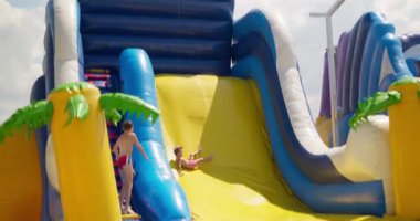 Pembe şortlu genç bir çocuk güneşli bir günde açık hava eğlence parkında şişme su kaydırağında eğlenceli bir gezinti yapıyor. Yüksek kalite 4k görüntü