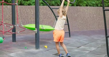 Parlak elbiseli genç, renkli yapılarla çevrili tırmanma ekipmanlarına asılarak modern bir oyun alanında aktif oyundan zevk alıyor. Yüksek kalite 4k görüntü