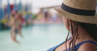 Saman şapkalı bir kadın, çocukları su parkında oynarken, rahatlama, yaz eğlencesi ve aile eğlencesi anlarını anımsıyor. Yüksek kalite 4k görüntü