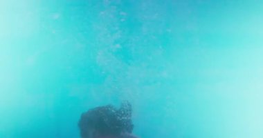 Küçük bir çocuk havuzda su altında, kırmızı gözlük takıyor ve yüzerken ayarlıyor, neşeli ve yaz manzarası yaratıyor. Yüksek kalite 4k görüntü