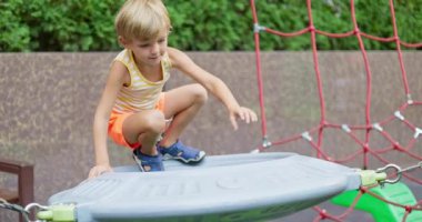 Renkli yaz kıyafetleri içindeki genç çocuk oyun parkına tırmanıyor aktif oyun, macera ve çocukluk eğlencesi sergiliyor. Yüksek kalite 4k görüntü