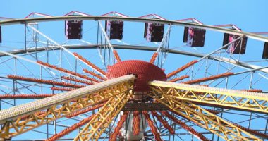 Kırmızı, sarı ve mor detaylara sahip canlı dönme dolap yapısı, mavi gökyüzü ile güneşli bir günde aşağıdan çekildi. Yüksek kalite 4k görüntü