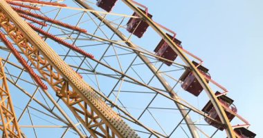 Dönme dolabın parlak metal çerçevesinin ve kulübelerinin açık mavi gökyüzüne doğru dönen yakın görüntüsü. Yüksek kalite 4k görüntü