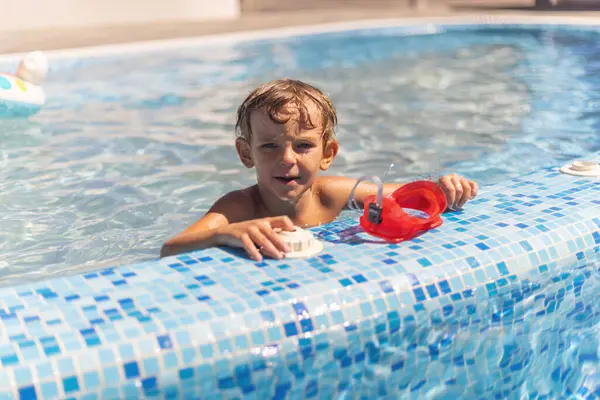 Havuz kenarında ıslak saçlı ve gün ışığında fayanslı yüzme havuzunda kırmızı gözlüklü bir çocuk.