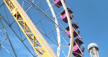 Kırmızı, sarı ve mor detaylara sahip canlı dönme dolap yapısı, mavi gökyüzü ile güneşli bir günde aşağıdan çekildi. Yüksek kalite 4k görüntü