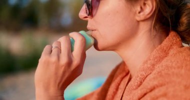 Açık havada, havluya sarılmış, plajda gün batımının sıcacık ışığında dinlenen bir kadın görüntüsü. Yüksek kalite 4k görüntü