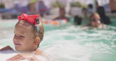 Alnında kırmızı gözlüklerle havuzda yüzen küçük bir çocuk. Etrafı su ve yaz güneşiyle çevrili. Yüksek kalite 4k görüntü