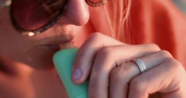 Altın saat içinde, güneş gözlüğü takan ve yumuşak ışıkta turuncu bir giysi giyen bir kadının yakın çekimi. Yüksek kalite 4k görüntü