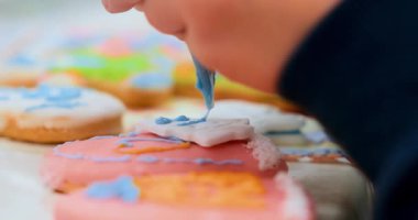 Kurabiyeleri renkli kremayla dekore eden birinin yakın çekim videosu. Sahne, tatil veya pişirme temalı içerik için ideal olan krema sürecinin karmaşık ayrıntılarını yakalıyor.
